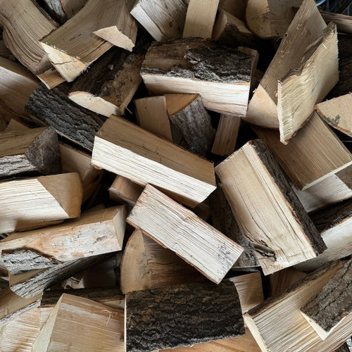 A pile of hardwood firewood logs and split with visible natural bark, light tan wood grain, and darker brown sections.