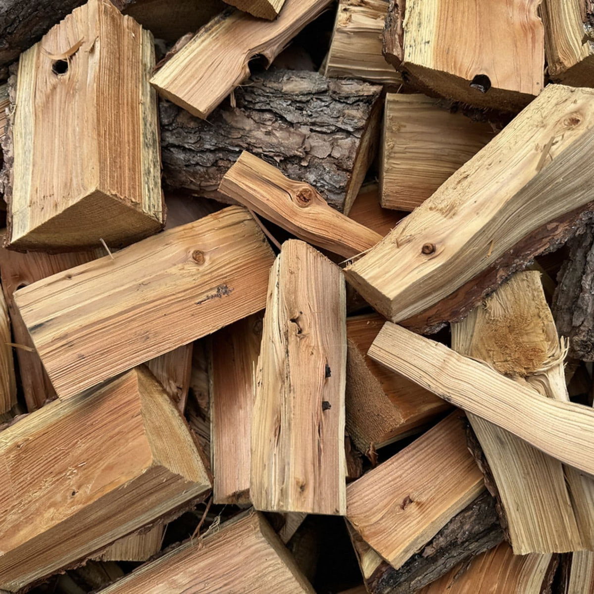 A close-up pile of cut kiln-dried firewood logs and split wood pieces with visible bark.