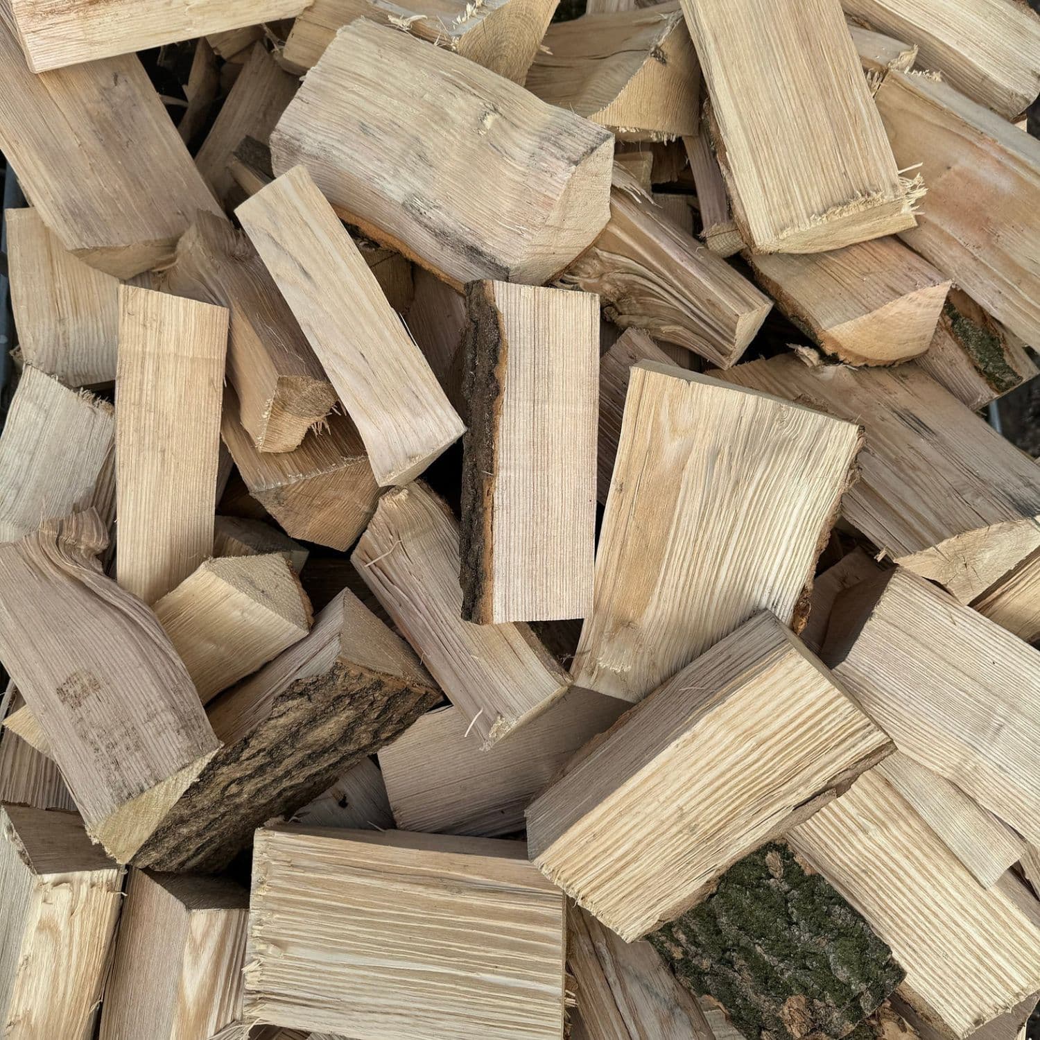 A pile of unseasoned cut hardwood firewood logs and split timber pieces stacked together.
