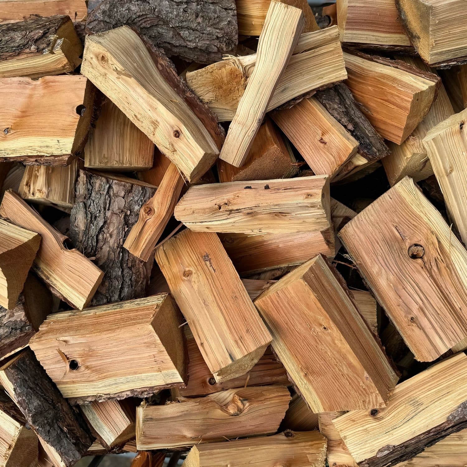 A close-up pile of cut unseasoned softwood firewood logs and split wood blocks.